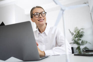 Thoughtful mature businessman sitting in front of laptop at desk in office - VPIF07800