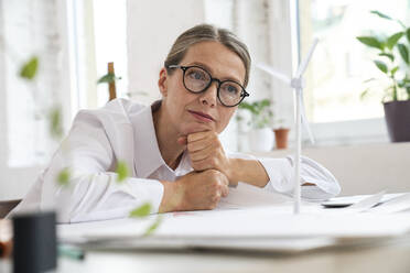 Thoughtful businesswoman with wind turbine on table in office - VPIF07810