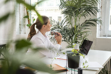 Reife Geschäftsfrau mit Brille sitzt am Tisch im Büro - VPIF07815