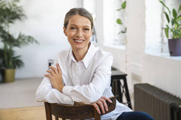 Happy mature businesswoman sitting on chair in office - VPIF07822