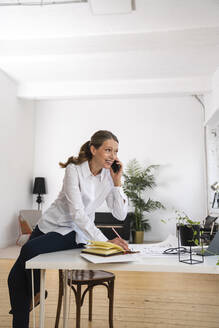 Glückliche reife Geschäftsfrau, die über ein Mobiltelefon spricht und auf einem Schreibtisch im Büro sitzt - VPIF07826