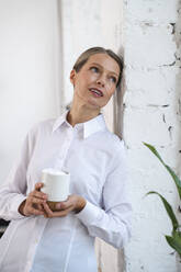 Kontemplative reife Geschäftsfrau mit Kaffeetasse an die Wand gelehnt - VPIF07830
