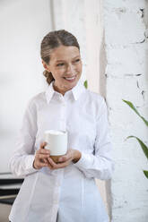 Happy mature businesswoman with coffee cup standing by wall - VPIF07831