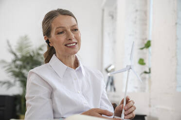 Smiling businesswoman holding wind turbine in office - VPIF07839