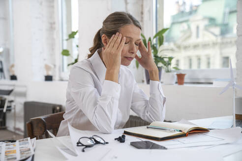 Frustrated businesswoman with head in hands sitting at office - VPIF07844