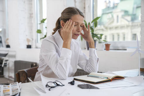 Frustrierte Geschäftsfrau mit dem Kopf in den Händen sitzt im Büro - VPIF07844
