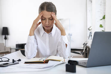 Exhausted businesswoman with head in hands sitting in office - VPIF07845