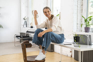 Happy mature businesswoman with wireless headphones sitting on desk - VPIF07850