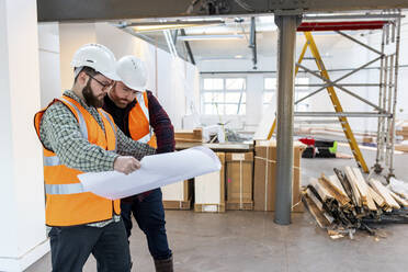 Young engineers discussing over blueprint at construction site - WPEF06928