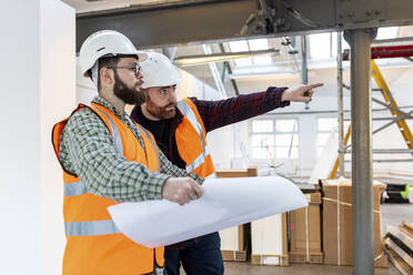 Junger Ingenieur gestikuliert und diskutiert mit einem Kollegen auf der Baustelle - WPEF06929