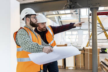 Young engineer gesturing and having discussion with colleague at construction site - WPEF06929