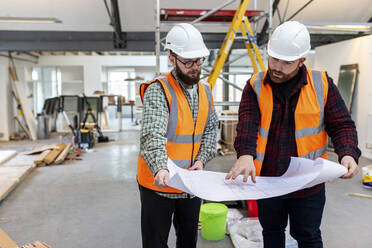 Ingenieur, der mit einem Kollegen auf der Baustelle über einen Bauplan diskutiert - WPEF06930