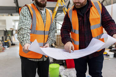 Ingenieure in reflektierender Arbeitskleidung diskutieren auf einer Baustelle über einen Bauplan - WPEF06932