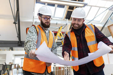 Zufriedener Ingenieur mit einem Kollegen, der auf einer Baustelle über einen Bauplan diskutiert - WPEF06933