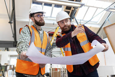 Ingenieur gestikuliert und diskutiert mit einem Kollegen auf der Baustelle - WPEF06934