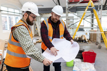 Junge Ingenieure mit Schutzhelm, die auf einer Baustelle über einen Bauplan diskutieren - WPEF06935