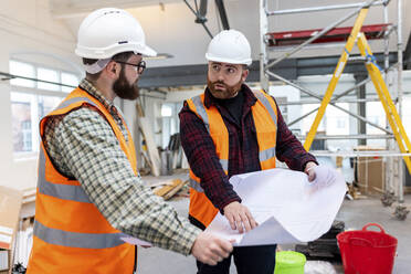 Junge Ingenieure in Arbeitsschutzkleidung diskutieren auf einer Baustelle über einen Bauplan - WPEF06936