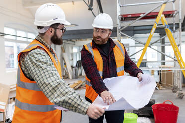 Young engineers wearing protective workwear discussing over blueprint at construction site - WPEF06936