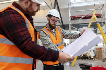 Engineer discussing over blueprint with colleague at construction site - WPEF06937