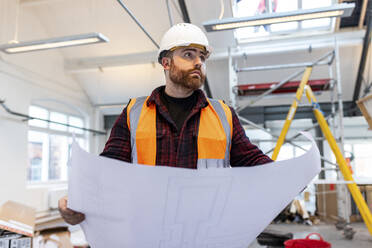 Young engineer standing with blueprint at construction site - WPEF06939