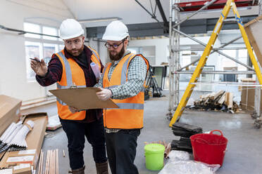 Junger Ingenieur gestikuliert und diskutiert über ein Dokument auf der Baustelle - WPEF06943