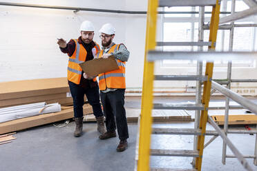 Young engineers examining and discussing over document at construction site - WPEF06946