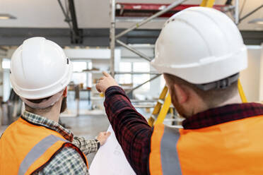 Young engineers wearing hardhat examining and having discussion at site - WPEF06950