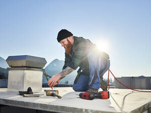 Dachdecker bei der Arbeit mit einer Zange auf dem Dach an einem sonnigen Tag - CVF02201