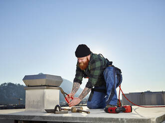 Dachdecker bei der Arbeit mit einer Zange an einem sonnigen Tag - CVF02205