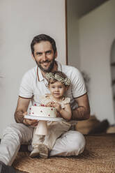 Lächelnder Vater und Tochter halten Geburtstagstorte zu Hause - MDOF00522
