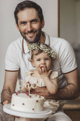 Lächelnder Vater mit Tochter, die einen Geburtstagskuchen zu Hause hält - MDOF00525