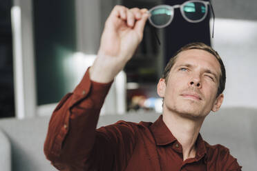 Businessman looking at eyeglasses in office - JOSEF15761