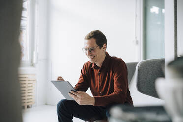 Happy businessman using tablet PC in office - JOSEF15816