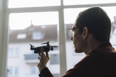 Businessman examining drone in front of window at office - JOSEF15830