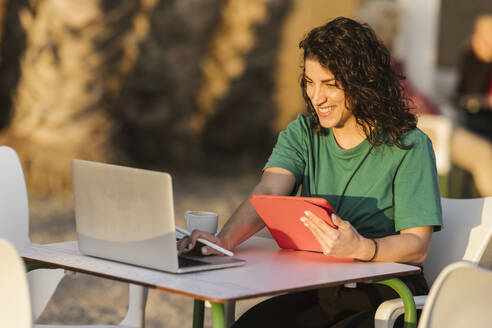 Happy woman using laptop sitting at outdoor cafe - LJF02468
