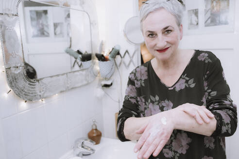 Smiling senior woman applying hand cream in bathroom - NGF00769