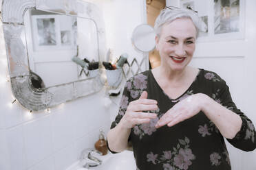 Glückliche Frau trägt im Badezimmer Feuchtigkeitscreme auf die Hand auf - NGF00770
