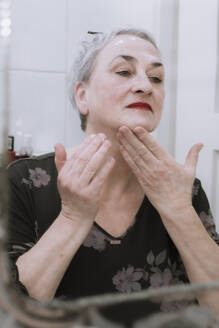 Senior woman applying face cream looking in mirror at bathroom - NGF00774