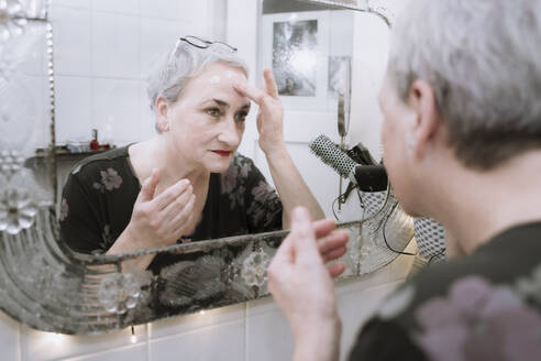 Reflection of senior woman applying face cream in bathroom - NGF00775