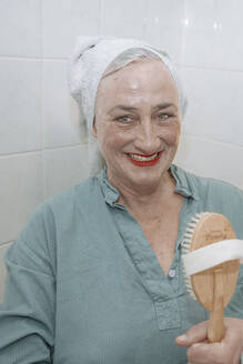 Happy senior woman holding wooden brush in bathroom - NGF00777