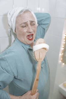 Senior woman with wooden brush singing in bathroom - NGF00778