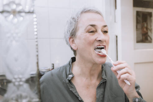 Senior woman brushing teeth in bathroom - NGF00779