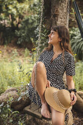 Young woman with hat sitting on swing at backyard - PCLF00206