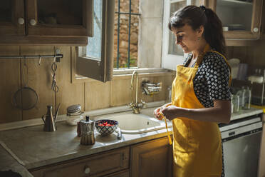 Junge Frau in gelber Schürze steht an der Küchentheke - PCLF00211