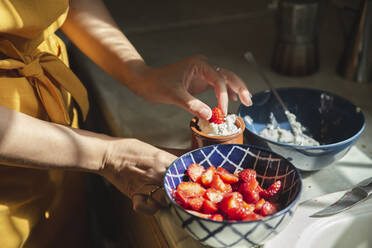 Hands of woman dipping strawberries in cream at kitchen - PCLF00213