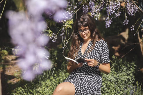 Woman wearing eyeglasses reading book in backyard - PCLF00217