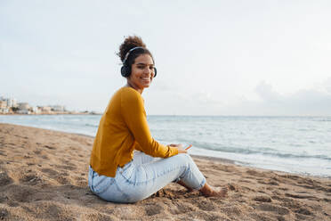 Glückliche Frau mit drahtlosen Kopfhörern, die am Strand Musik hört - JOSEF15840