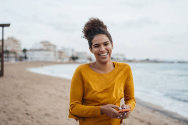 Happy young woman with mobile phone standing at shore - JOSEF15880