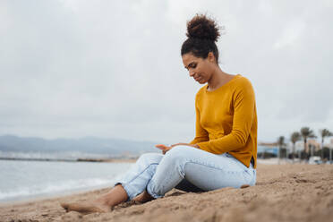 Junge Frau mit Mobiltelefon auf Sand sitzend - JOSEF15888