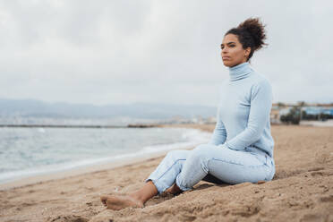 Nachdenkliche junge Frau sitzt im Sand am Strand - JOSEF15890